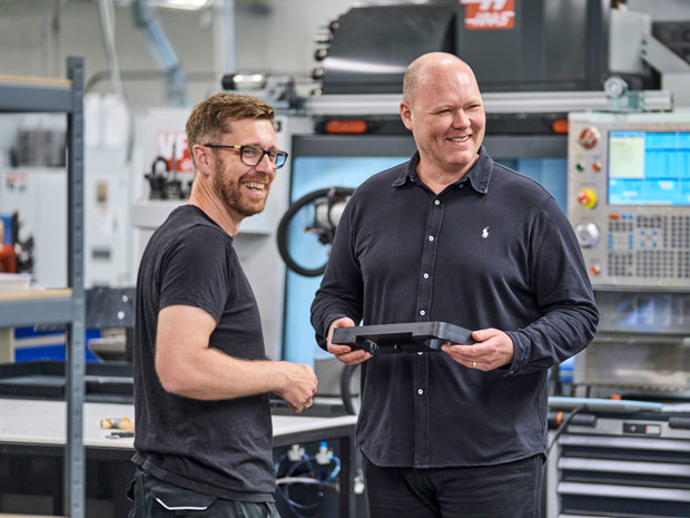 To kolleger fra Induflex står foran en drejebænk og snakker om et plastemne.