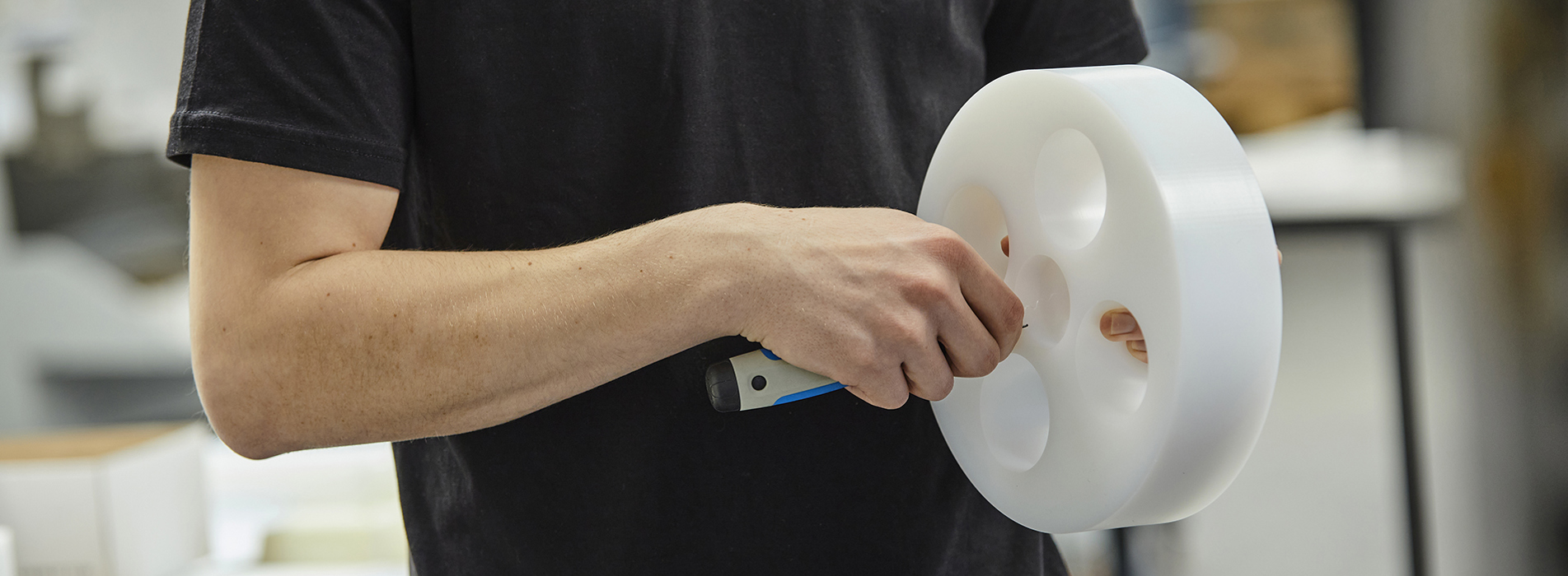 Drejet emne med fire huller i hvid POM afgrates manuelt af Induflex' industritekniker