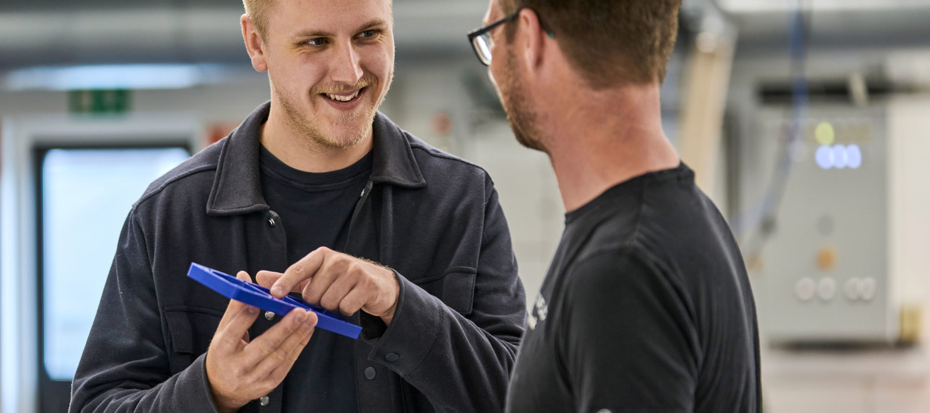 En sælger peger på et blå plastemne foran en industritekniker. 