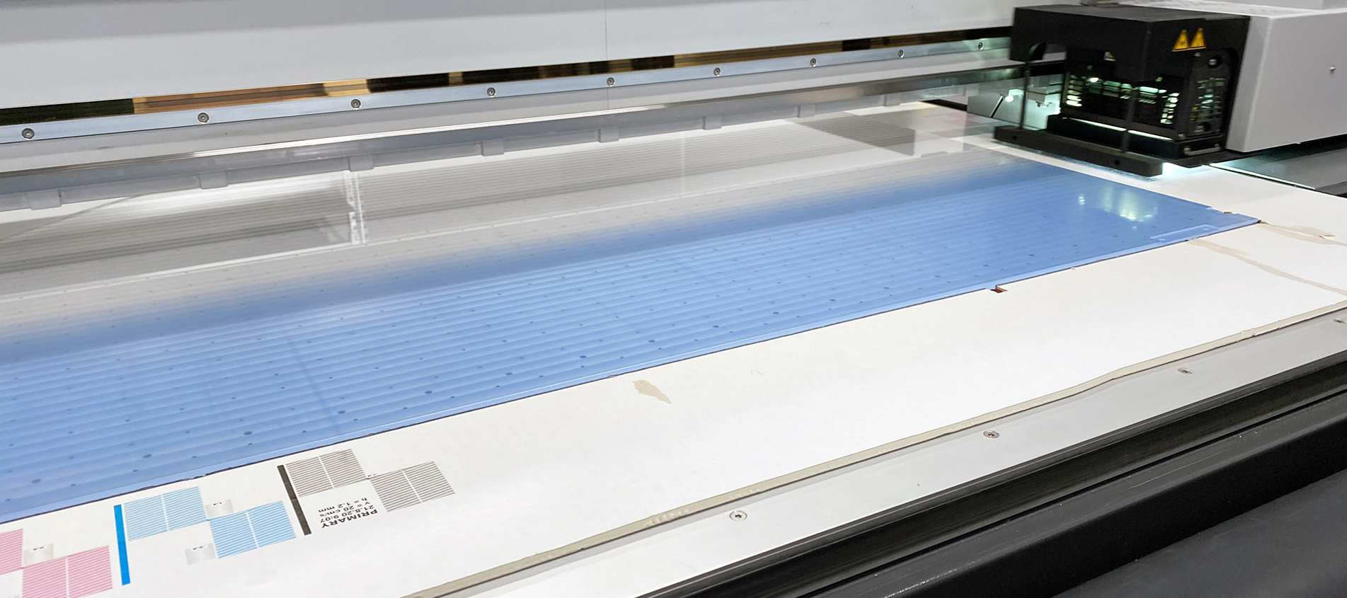 Digitalprinter er i gang med at printe lyseblå print på en gennemsigtig akrylplade