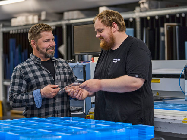 To employees inspect a batch of transparent, laser cut plastic parts.