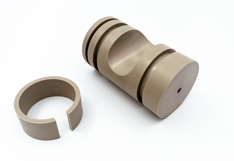 To CNC-drejede emner i PEEK på en hvid baggrund.