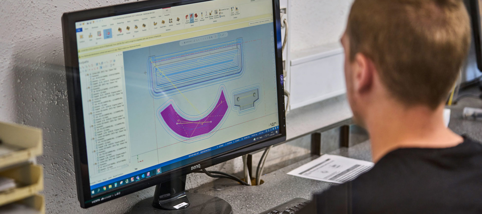 En industritekniker programmerer en maskine ved en computer. 