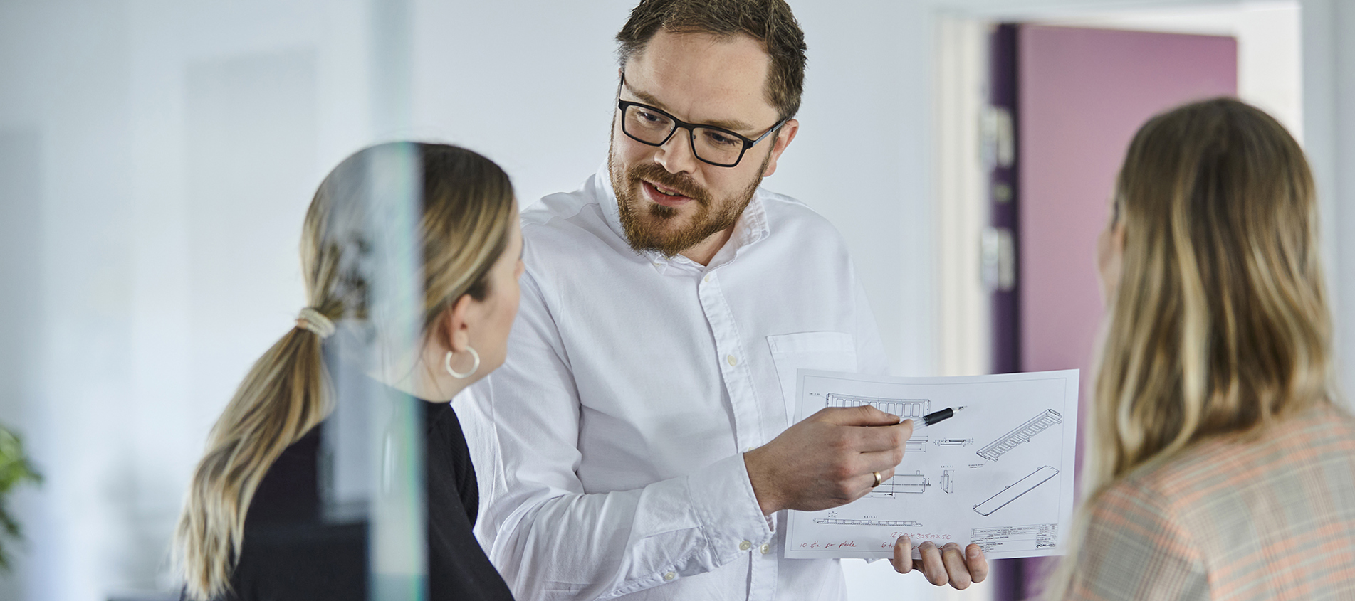 Tre sælgere hos Induflex diskuterer detaljer på en teknisk tegning af et plastemne til en kunde