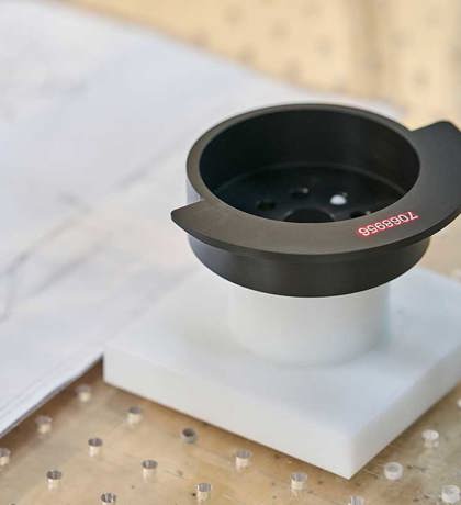 A black turned machine part with laser engraved numbers.