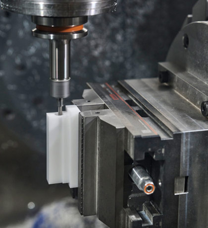 En hvid maskindel i POM fræses i en CNC-fræser.