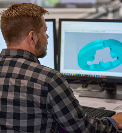 A technical designer adjusts a design of a machine part og plastics on his computer screen.