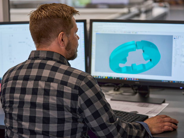 A technical designer adjusts a design of a machine part og plastics on his computer screen.