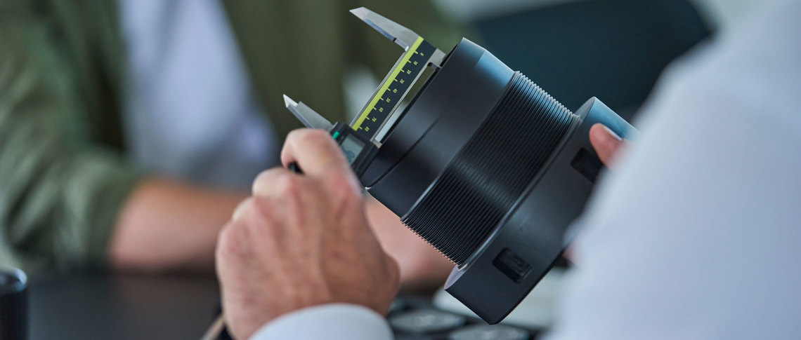 En sort drejet maskindel i plast måles med en skydelære. 