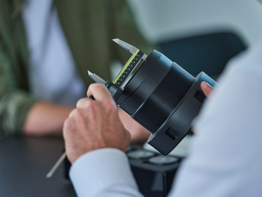 En sort drejet maskindel i plast måles med en skydelære. 
