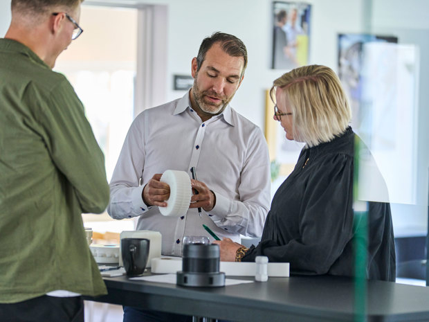 A salesperson shows a customer a white machine part made from plastics. 