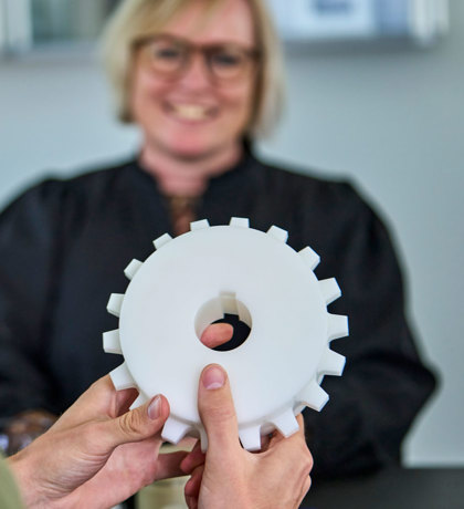 An employee holds a white machine part in his hands during a meeting. 
