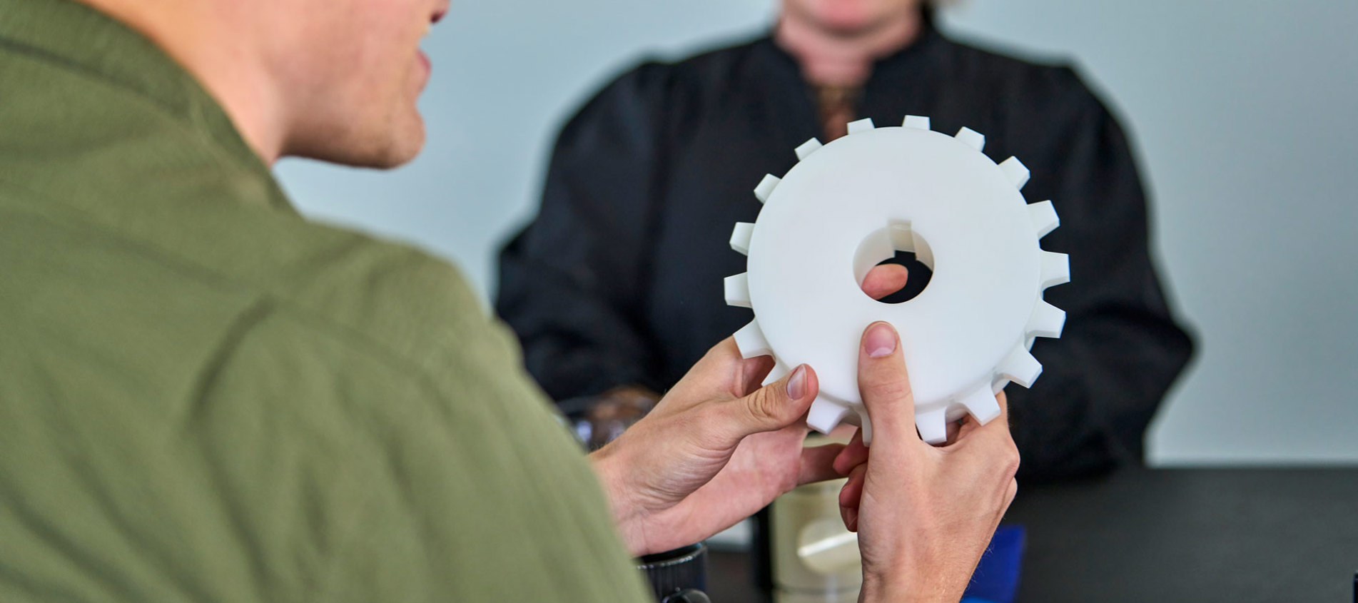 En medarbejder holder en hvid maskindel i sine hænder til et møde. 