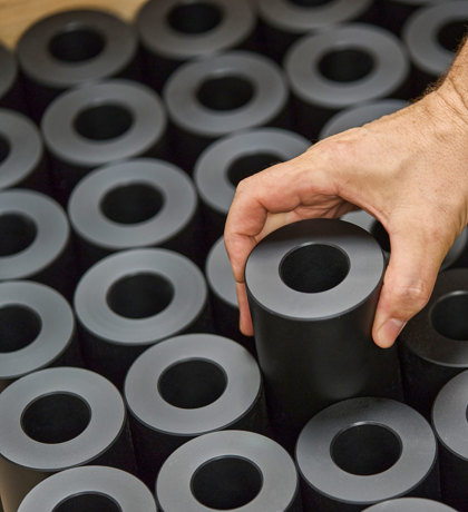 A hand lifts a turned machine part in black plastics from a pallet filled with machine parts.  
