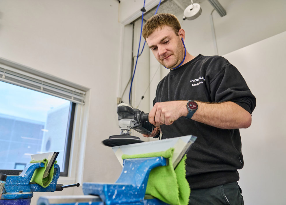 En medarbejder polerer et stykke akryl manuelt med en poleringsmaskine. 