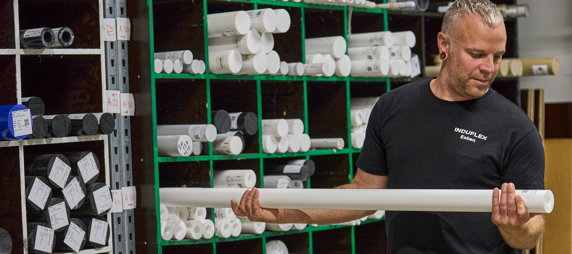 En industritekniker tager en plaststang ud fra en reol med stænger. 