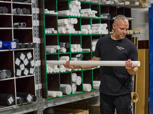 An industrial technician takes out a plastic rod from a shelving unit.