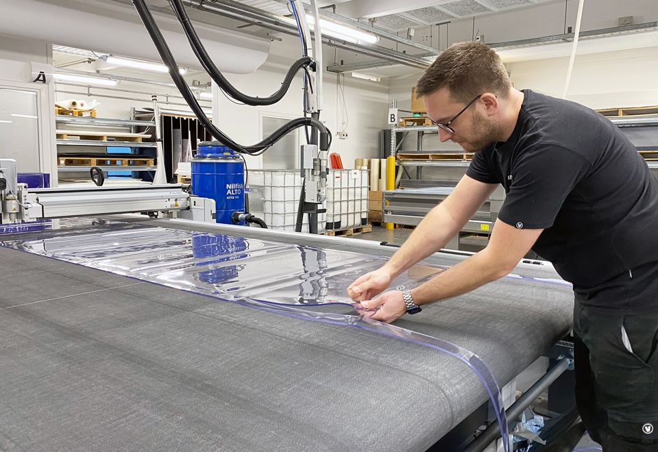 En produktionsmedarbejder tjekker en udskæring af blød PVC på en skæreplotter