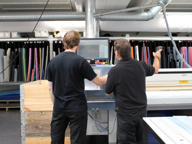 To industriteknikere står ved skærmen på en laserskærer som de er ved at klargøre