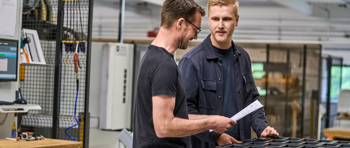 En sælger og en industritekniker tjekker et plastemne i produktionen. 