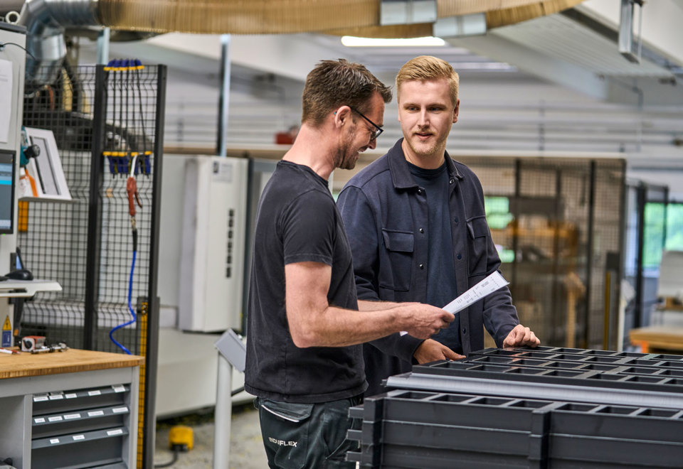 En sælger og en industritekniker tjekker et plastemne i produktionen. 